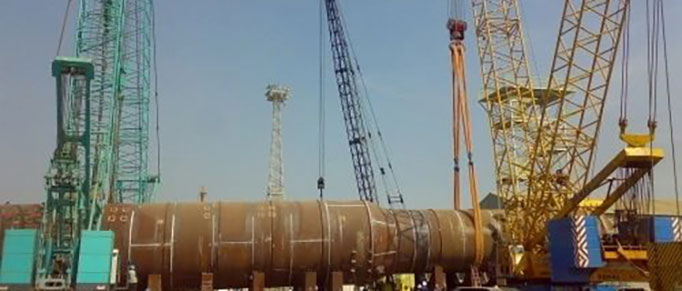 A series of slings and rigging lowering a massive pipe into place.