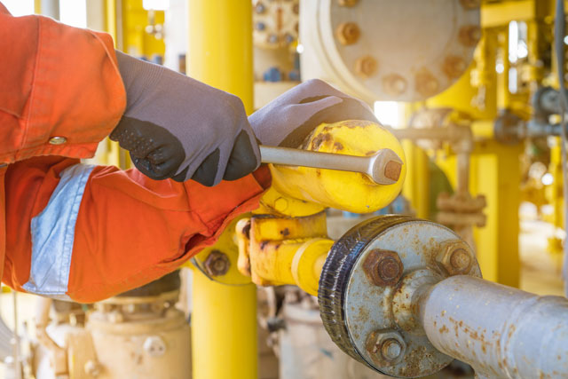 A rig worker tightening a yellow pipe.