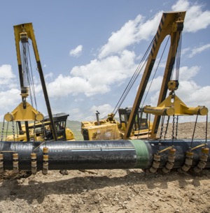 Cranes lowering an oil pipe into the ground.