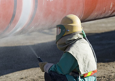 A worker sprays down a large orange pipe outside.
