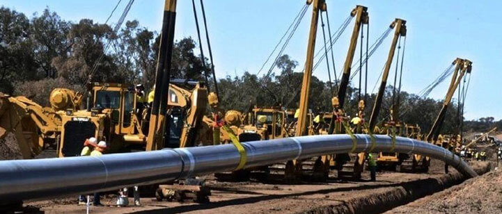 A series of cranes lowering a pipe into a trench.